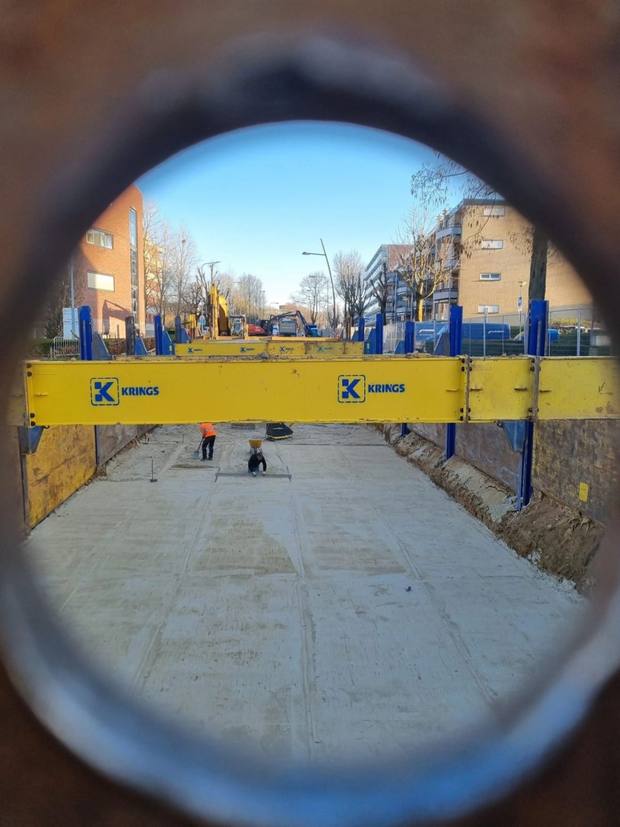 Doorkijk door een buis naar een bouwput met damwanden