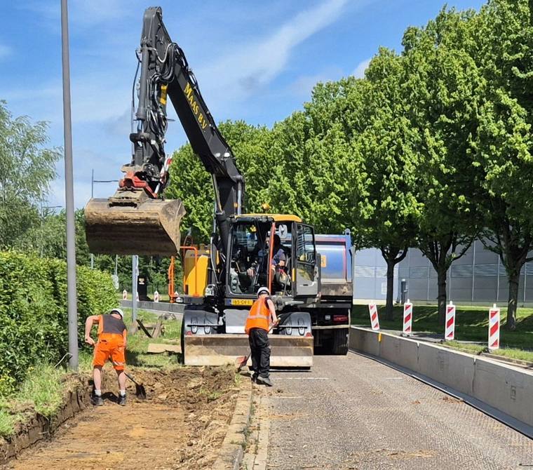 Graafmachine en wegwerkers bij groot asfaltonderhoud langs een laan met bomen